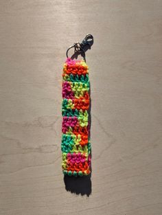 a crocheted keychain is laying on a wooden surface with a black hook