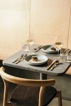 two plates with food on them sit on a table next to wine glasses and utensils