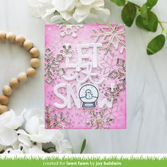 a card with snowflakes on it next to some white flowers and wood beads