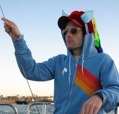 a man in a blue hoodie is holding a fishing pole while standing on a boat