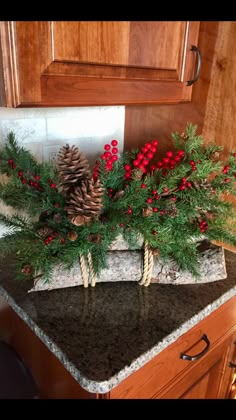 some pine cones and berries are sitting on a granite counter top in a kitchen with wood cabinets