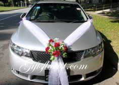 a wedding car decorated with red flowers and white ribbon tied to it's hood