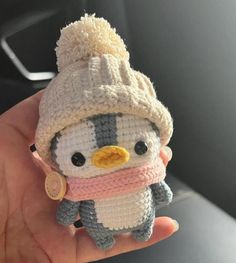 a small stuffed penguin wearing a knitted hat and scarf is held in someone's hand