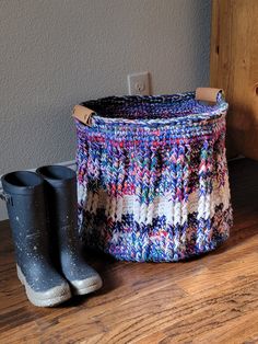 a pair of rubber boots sitting next to a knitted basket on a wooden floor