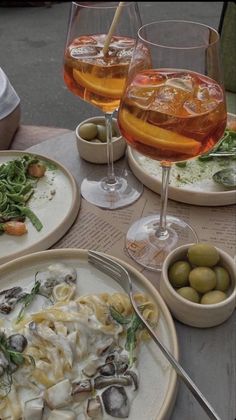 two glasses of wine and plates of food on a table with utensils,