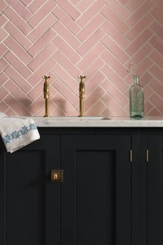 two faucets are on top of a black cabinet in front of a pink tiled wall