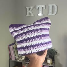 a person holding up a purple and white crocheted pillow in front of a bookcase