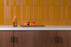 a vase with flowers and apples on a counter top in front of a yellow tile backsplash