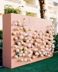 a pink and white sign with lots of balls hanging from it's sides in front of a palm tree