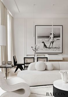 a living room filled with white furniture next to a painting on the wall above a coffee table