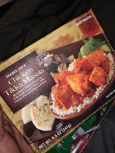 a person holding up a packet of chicken tikka masala with rice and vegetables