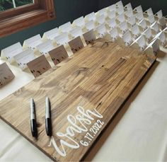 a wooden cutting board with place cards and pens on it, sitting on a white table cloth