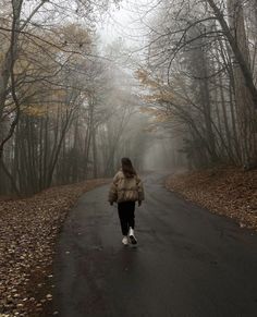 a woman walking down a road in the woods on a foggy day with lots of trees