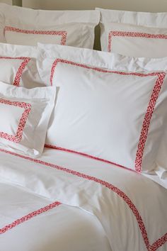 a bed with white sheets and red trimmings on the pillowcase is shown