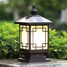 a light that is sitting on top of a cement block in front of some bushes