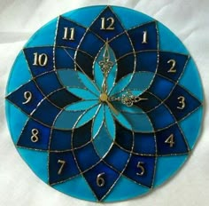 a blue clock with gold numbers and a flower design on the face is sitting on a white sheet