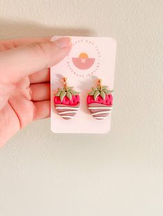 a hand holding a pair of strawberry shaped earrings