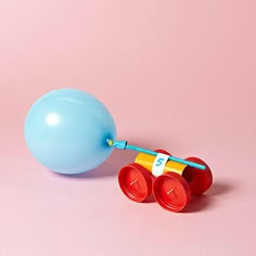 a blue ball and two red cups on a pink surface with a balloon attached to it