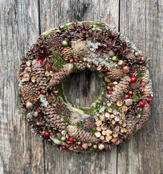 a wreath with pine cones and berries hanging on a wooden door, covered in moss