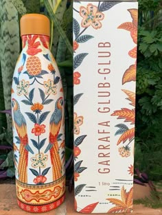 an orange and white ceramic bottle next to a cardboard box with flowers on the outside