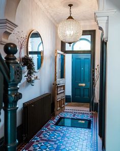 a hallway with blue and red tiles on the floor next to a black door, two round mirrors hanging from the ceiling