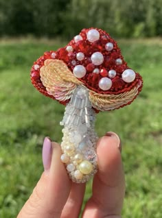 a hand holding a red and white brooch with pearls on it's end