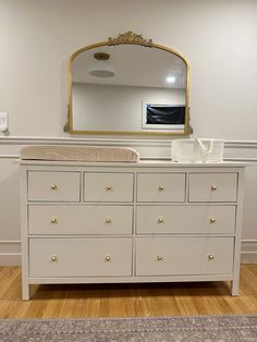 a white dresser with gold handles and a mirror on the wall above it in a room