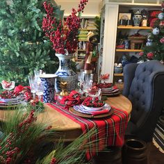 a dining room table set for christmas with red and blue dishes on it, surrounded by greenery