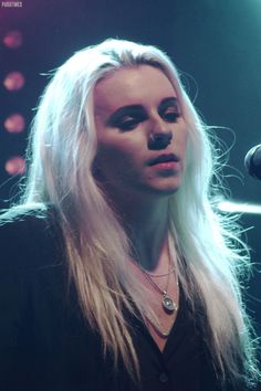 a woman with long blonde hair standing in front of a microphone