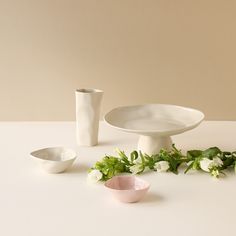 a white table topped with two plates and bowls filled with flowers next to each other