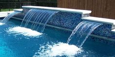 an outdoor swimming pool with water features and blue tiles on the walls, along with two benches