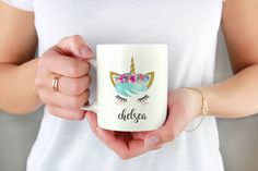 a woman is holding a coffee mug with a unicorn face and flowers on the front