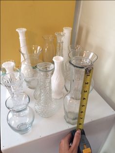 a person is measuring glass vases on a table with a tape measure in front of them