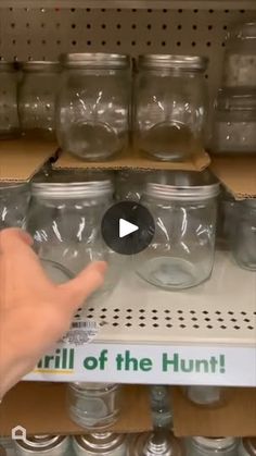 a person is pointing at some jars on the shelf in front of other shelves with one hand