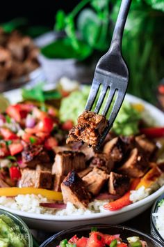 a fork is stuck into a plate of meat and rice with guacamole