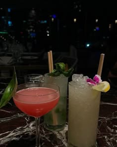 two cocktails sitting on top of a table next to each other with drinks in front of them