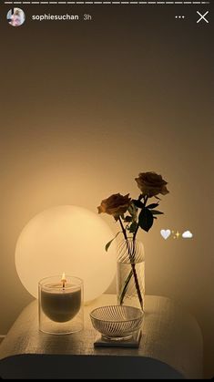 a glass vase with flowers and a lit candle on a table in front of it