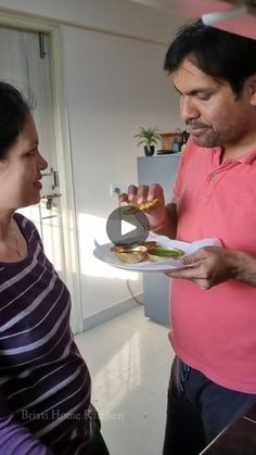 a man holding a plate with food on it while standing next to a woman in a kitchen