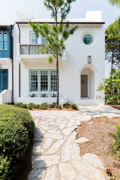 a white house with blue shutters on the front and side windows, surrounded by greenery