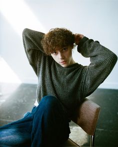 a young man sitting in a chair with his hands on his head and looking at the camera