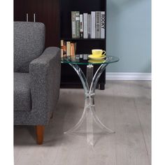 a glass table with a yellow plate on it in front of a gray chair and bookcase