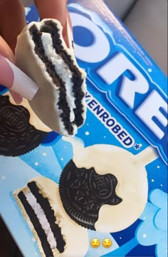 a hand holding a piece of cake with oreo cookies on it and an oreo sandwich in the background