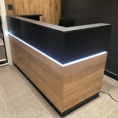 an office reception desk with black and wood paneling on the front, light up at the top