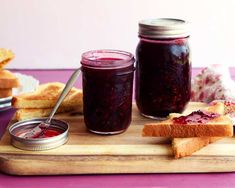 two jars of jam sitting on top of a wooden cutting board next to slices of bread