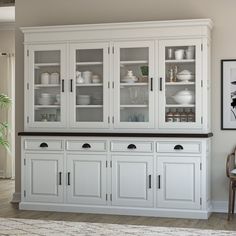 a white china cabinet with glass doors and drawers in a living room next to a rug