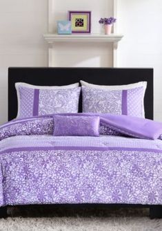 a bed with purple and white comforters in a room