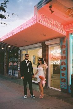 a man and woman are standing in front of a building with neon lights on it