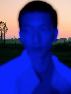 a blurry photo of a man in a blue shirt and tie at dusk with the sun setting behind him