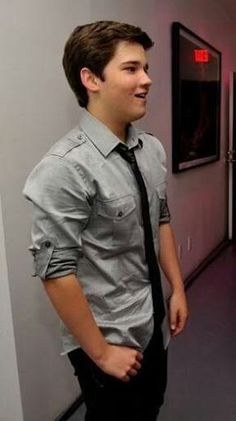 a young man wearing a tie standing in an office hallway