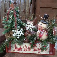 a snowman sitting on top of a wooden box filled with christmas decorations